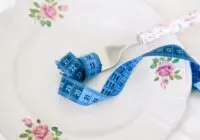 A floral plate with a fork and blue measuring tape symbolizing dieting or healthy eating.