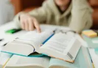 A person pointing at an open book on a desk, focusing on learning.