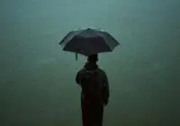 A person stands alone in the rain, holding an umbrella, creating a moody atmosphere.