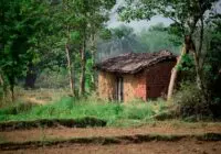 A quaint clay and brick house nestled in a verdant rural landscape surrounded by trees and greenery.