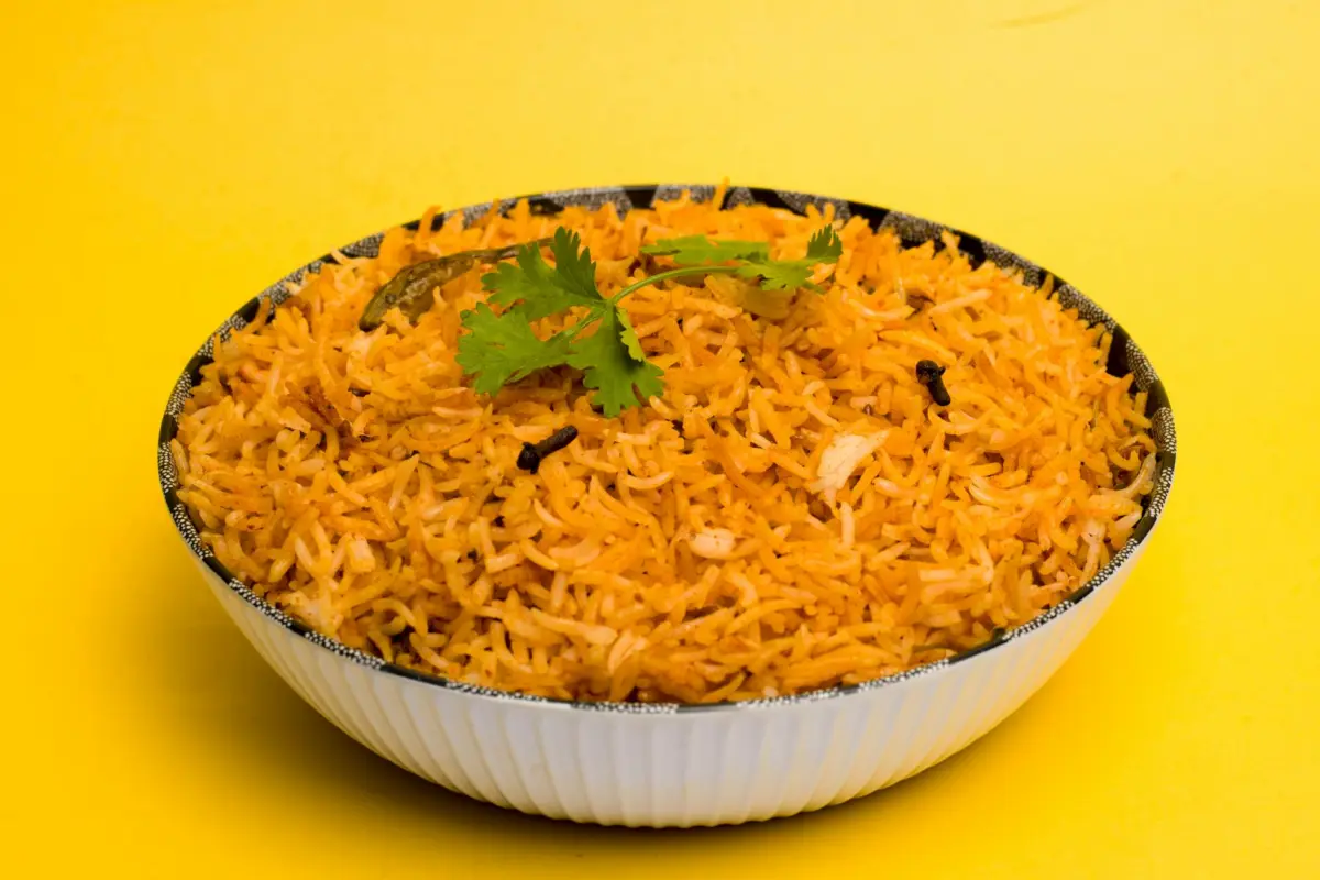 Aromatic Indian biriyani with spices served in a white bowl with a vibrant yellow background.