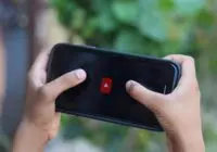 Close-up of hands holding a smartphone displaying a video app icon outdoors.