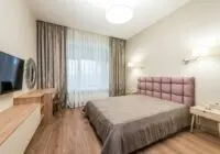 Contemporary bedroom with TV and curtains decorating window under bright luminous round shaped lamps