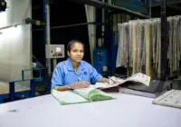 Female textile worker in factory reviewing documents at a desk.