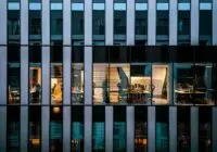Illuminated office inside a modern glass building exterior, showcasing architecture and workspace design.