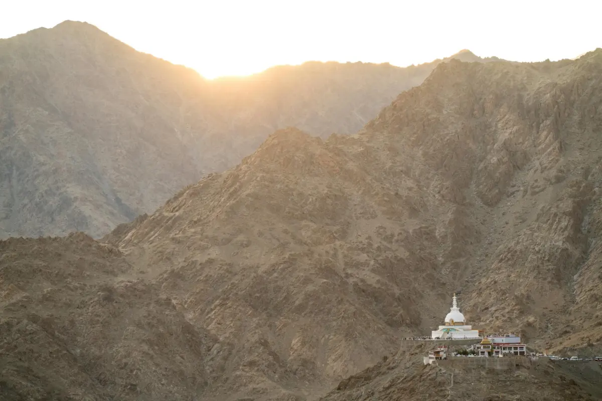 Serene view of Shanti Stupa with rugged mountains at sunrise, highlighting natural beauty.