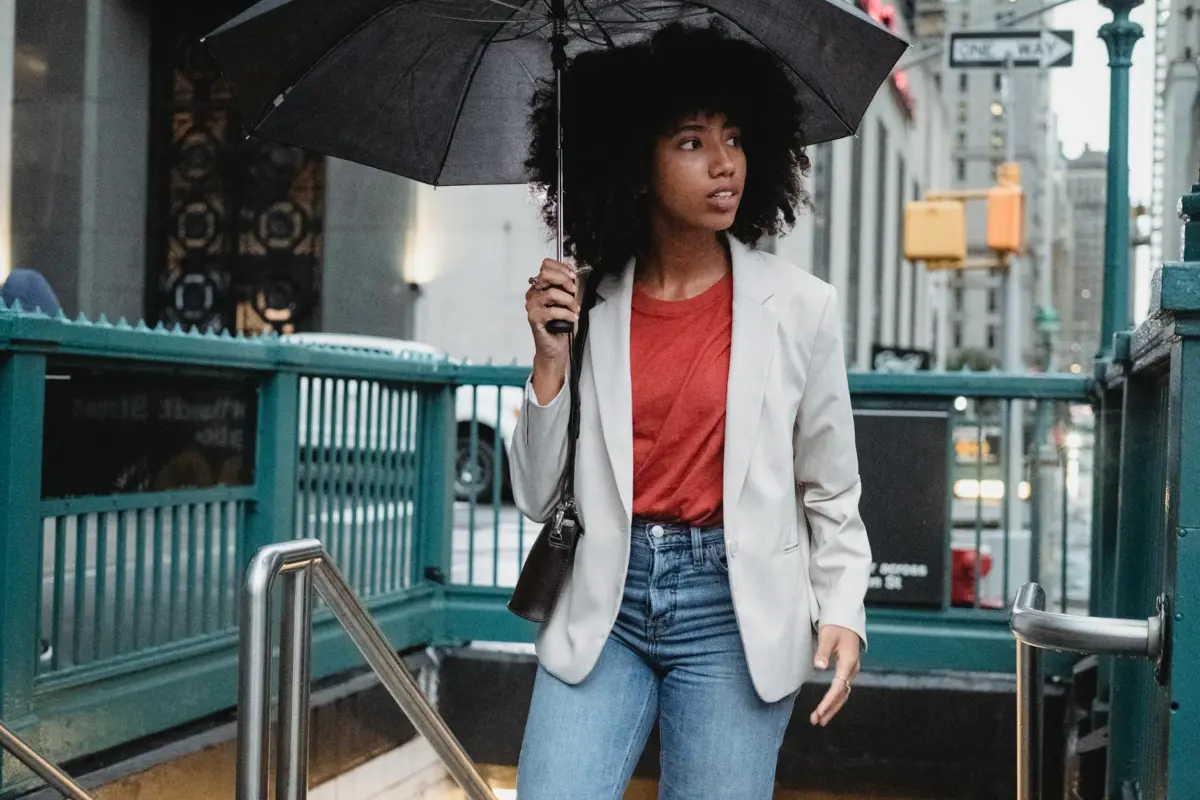 Woman walking on city street holding an umbrella, stylish attire.