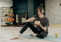 Young woman enjoying a healthy salad after exercising indoors. Promotes a balanced diet and fitness lifestyle.