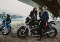 A couple sharing a moment on motorcycles underneath a modern bridge.