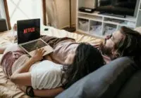 A cozy couple lounging in bed, streaming Netflix together on a laptop, enjoying a peaceful moment.