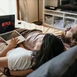 A cozy couple lounging in bed, streaming Netflix together on a laptop, enjoying a peaceful moment.