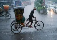 A cycle rickshaw driver maneuvers through heavy rain on an urban street, showcasing resilience and daily city life.