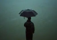 A person stands alone in the rain, holding an umbrella, creating a moody atmosphere.