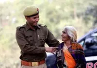 A smiling Indian police officer assists an elderly woman outdoors, showcasing community care.