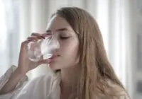 A woman enjoying a refreshing glass of water indoors during the day.