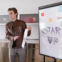 A young entrepreneur gives a presentation on startup strategies indoors with a flip chart.