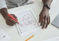 Close-up of a teacher marking a test paper with a red marker on a desk.