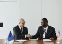 Corporate handshake between diverse businessmen representing EU and US flags, symbolizing partnership and collaboration.