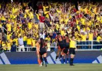 Energetic crowd of Colombian football fans cheering at a match in a vibrant stadium.