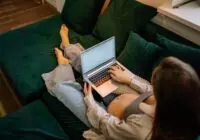 Pregnant woman sitting comfortably on a sofa using a laptop, working remotely.