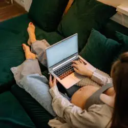 Pregnant woman sitting comfortably on a sofa using a laptop, working remotely.