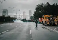 Tense urban scene showing police presence in riot gear amidst smoke during a protest.
