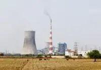 A cooling tower and smokestack in rural India, highlighting industrial and environmental contrasts.