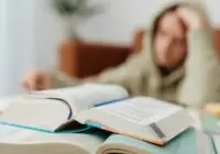 Blurred student studying at desk with open books, showcasing academic stress.