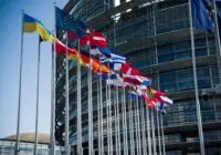 Flags of European Union countries outside a modern building facade.