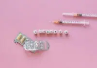 Flat lay of diabetes medication symbolized with pills and syringes on a pink background.