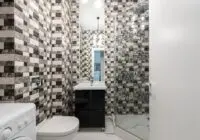 Interior of bright washroom with washing machine near toilet next to shower and sink with tap