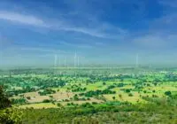 A stunning view of wind turbines towering over vibrant green fields under a clear blue sky in Rajapur, India.