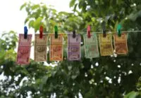 Colorful Indian rupee banknotes pinned and hanging on a clothesline against a green leafy backdrop.