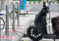 Electric scooter plugged into a charging station in a city environment, showcasing eco-friendly urban transportation.